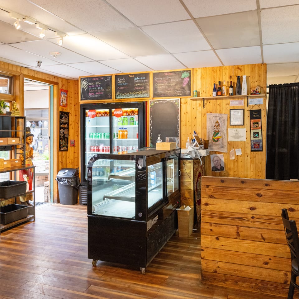 Interior of a restaurant with wooden walls, a display case, drink refrigerators, and a service counter.