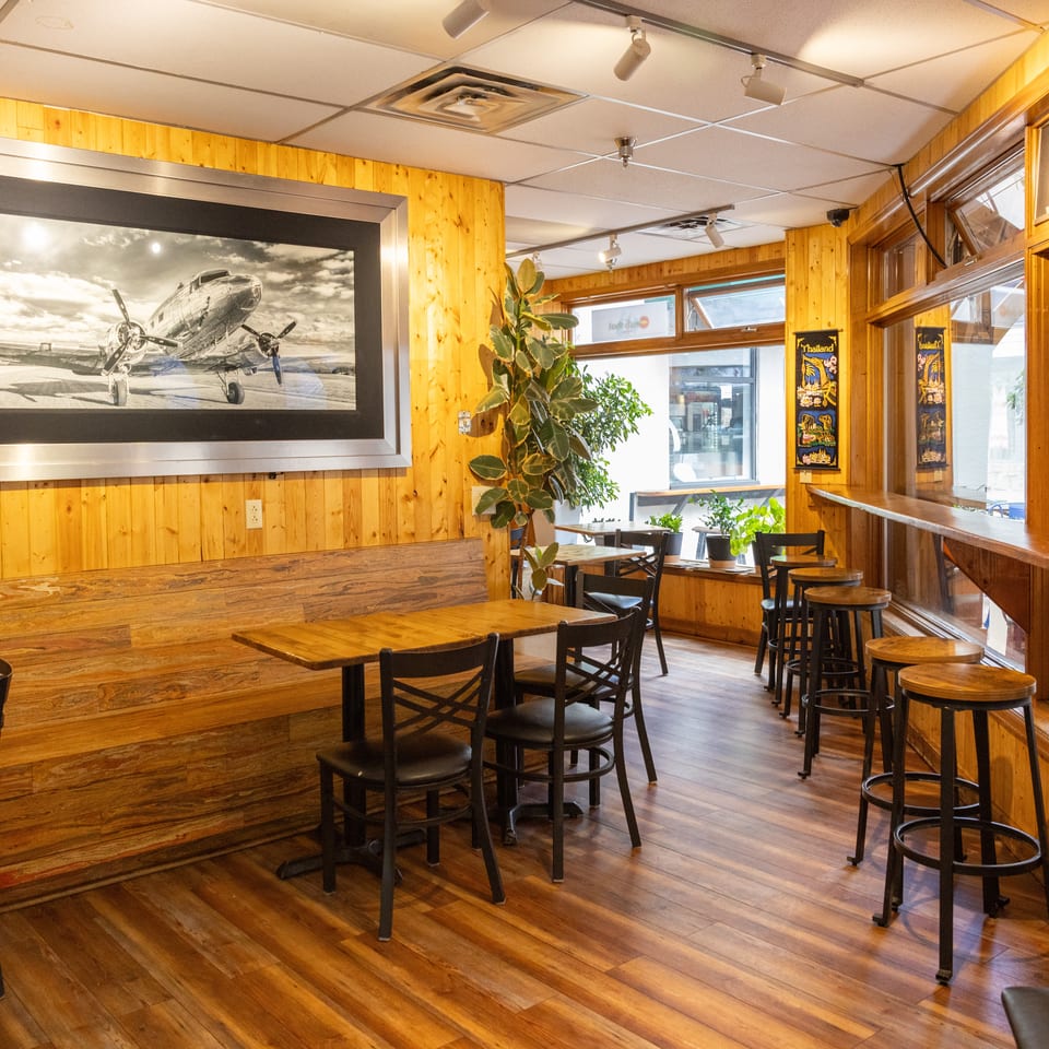 Cozy restaurant interior with wooden walls, tables, chairs, and a large framed airplane picture.