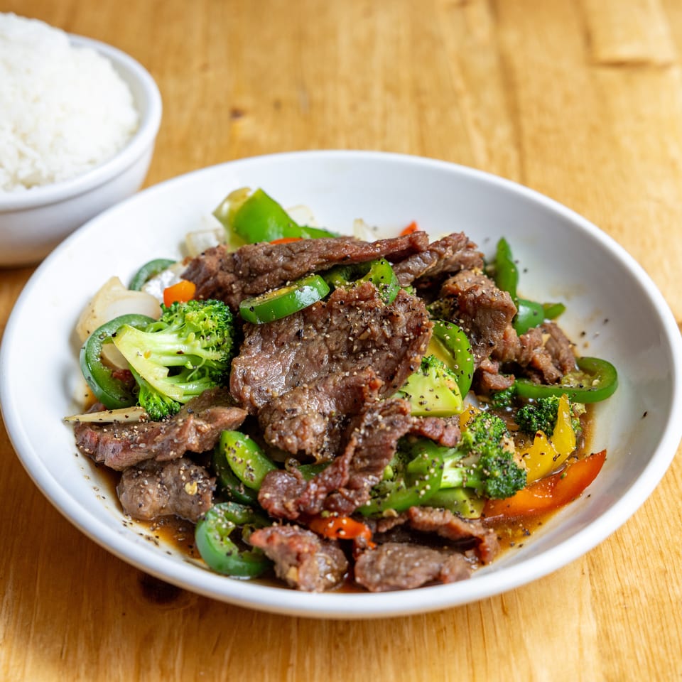 Stir-fried beef with broccoli, bell peppers, and jalapeños, served with a side of white rice.