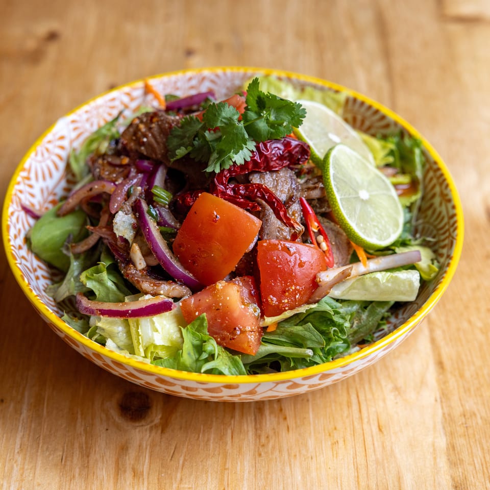 Spicy Thai beef salad with red onions, tomatoes, lime, and cilantro in a colorful bowl.