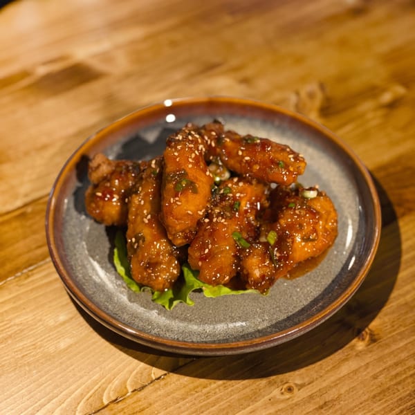 A plate of glazed chicken wings with sesame seeds and green onions on a wooden table.