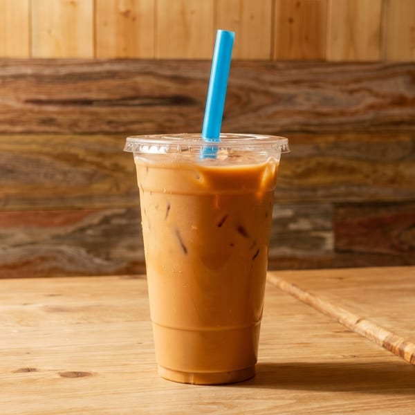 Iced coffee in a clear plastic cup with a blue straw on a wooden table.