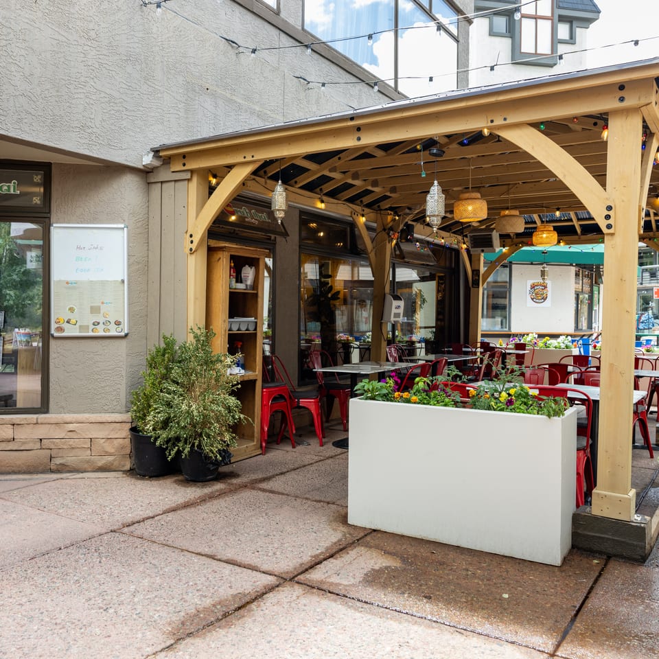 Outdoor patio of Grub Thai restaurant with red chairs, tables, and a wooden pergola adorned with string lights.