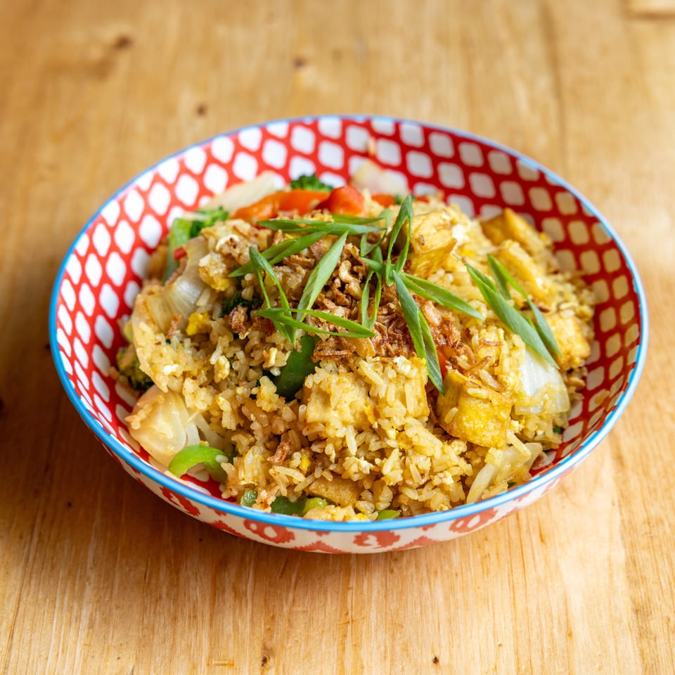 Fried rice with tofu, vegetables, crispy onions, and green onions in a patterned bowl.